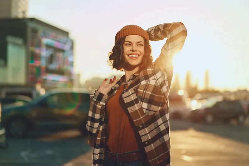 Woman portrait smiling in urban street at golden hour, candid lifestyle moment with golden hour glow, authenticity and mindful living captured in emotional storytelling mood.