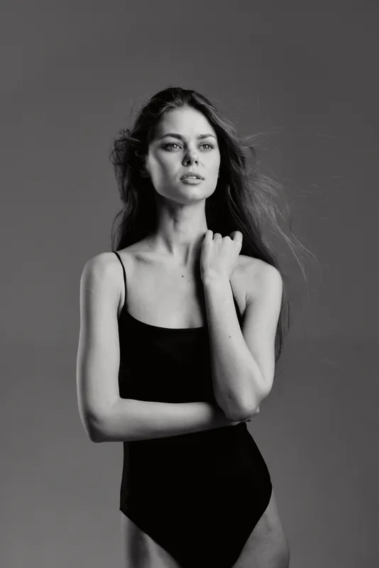 Black and white portrait of a confident woman wearing a black swimsuit with long hair and serious expression