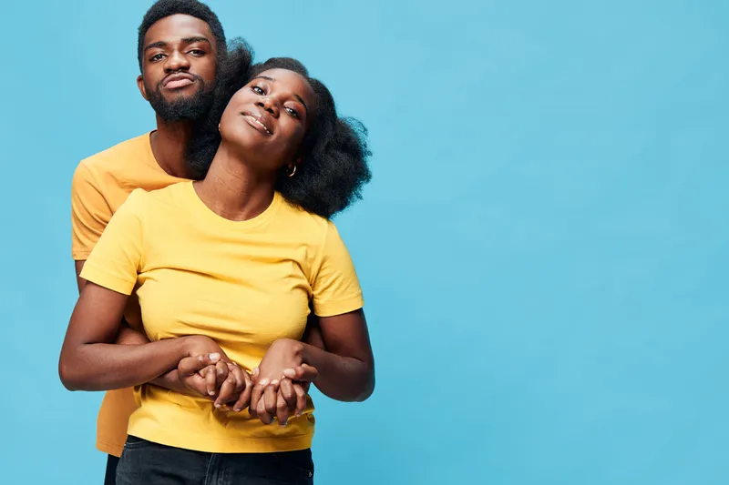 A joyful young African couple in matching yellow t shirts, posing playfully against a bright blue background, radiating love and happiness together
