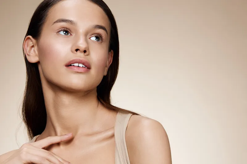 Beautiful young model with natural makeup, neutral background, exuding confidence and serenity, perfect for beauty and skincare themes