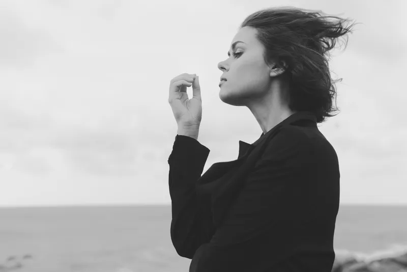 Woman in a blazer stands on a windy seashore in monochrome, outdoor mood, elegant pose, coastal atmosphere, cinematic silhouette and calm, reflective demeanor