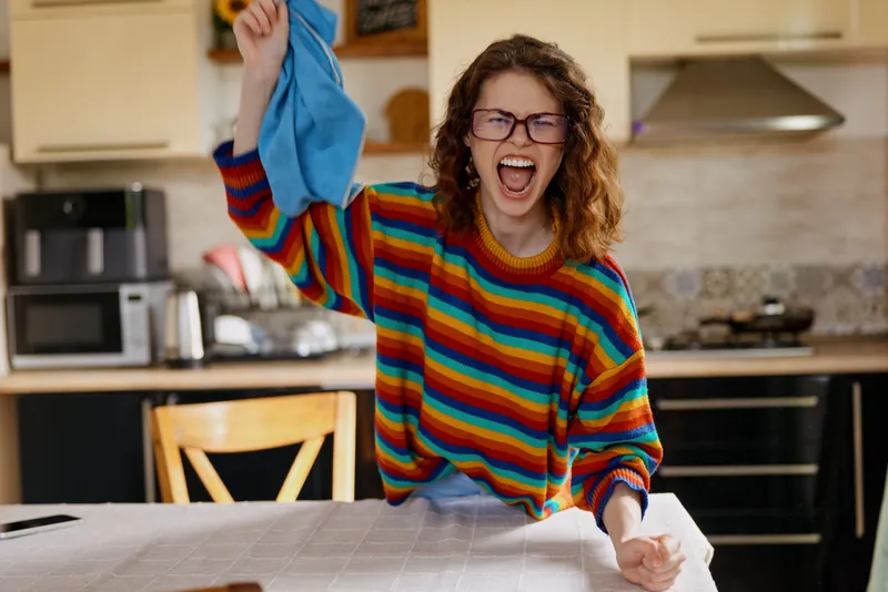 Joyful woman indoors, bright striped sweater, kitchen setting, laughing with open mouth, playful energy, casual home moment, natural light, vibrant colors, candid lifestyle. authentic vibe