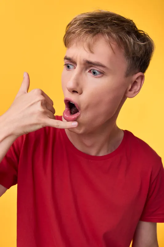 Surprised gesture with hand signaling call me against a bright yellow background, a man in a red shirt showing playful communication for social media and casual lifestyle content.