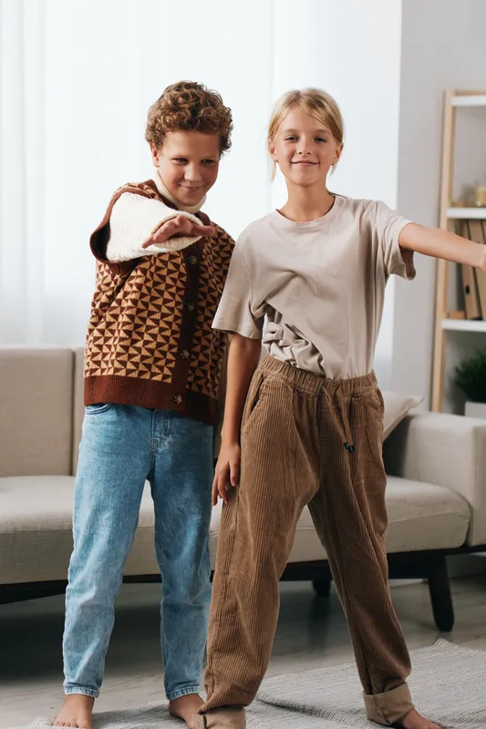 Authentic scene of two school age children dancing and laughing at home, illustrating genuine play and everyday lifestyle in a warm, candid indoor setting.