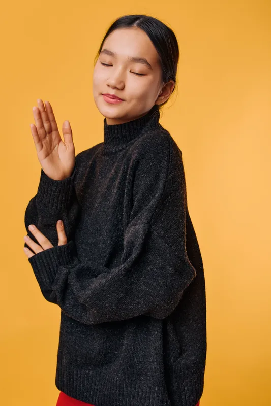 Young woman with closed eyes and relaxed face wearing black sweater on orange background. Calm expression, casual pose, peaceful mood, comfortable clothing for autumn or winter style.