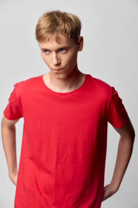 Teenage boy in a red t shirt stands in a studio with hands on hips, confident expression, casual fashion shoot, clean background, youth lifestyle and modern style photography