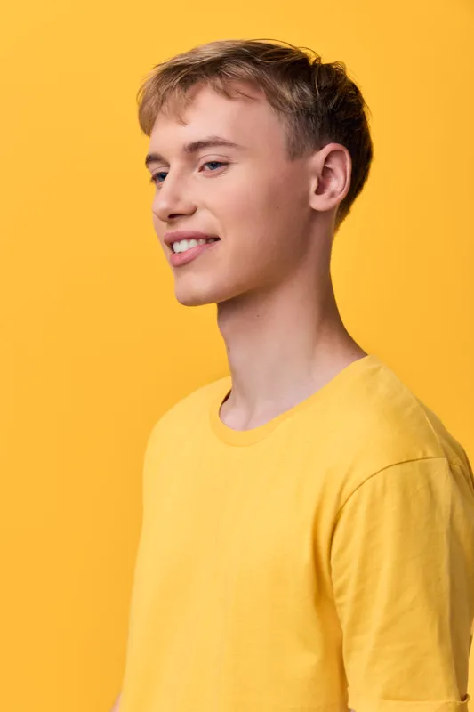 Smiling young man in a yellow shirt stands against a vibrant studio backdrop, casual style and relaxed pose for fashion, lifestyle, or branding imagery suitable for catalogs, campaigns and social