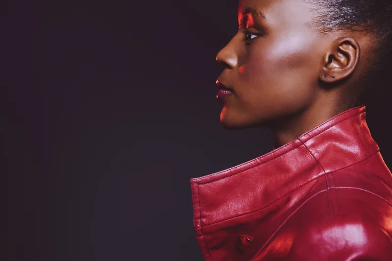 Profile of a dark skinned African woman wearing a red leather jacket on a black background. Concept of fashion, beauty, style, and confident female portrait with studio lighting.