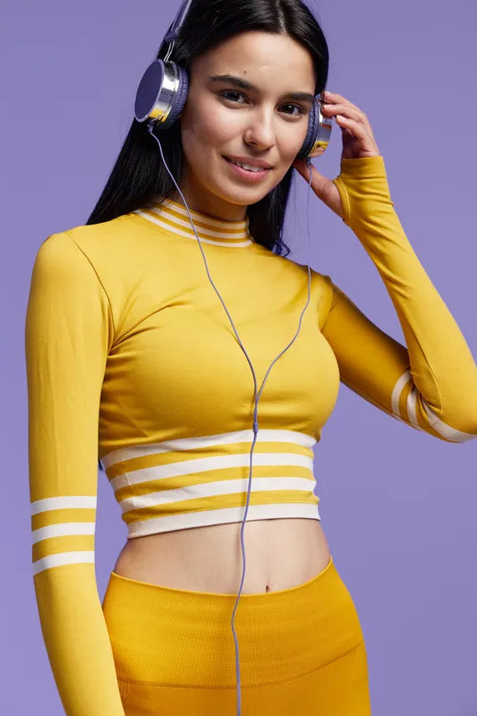 Sport fitness woman in a yellow outfit wearing headphones and smiling, standing against a purple background, focused on workout and healthy lifestyle.