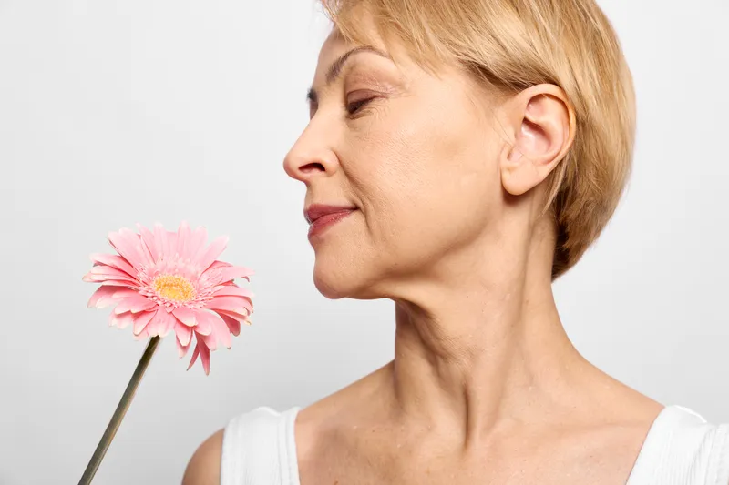 Elegant elderly woman in side profile, eyes closed softly smelling a pink flower, beauty and nature for relaxation and wellbeing, peaceful life