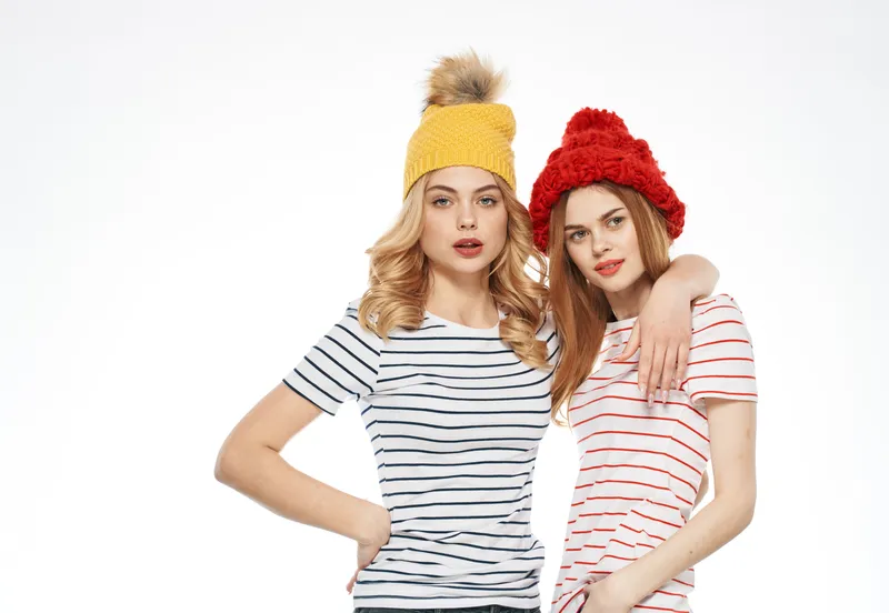 Милые подруги в модной одежде и разноцветных кепках обнимаются, крупный план, общение