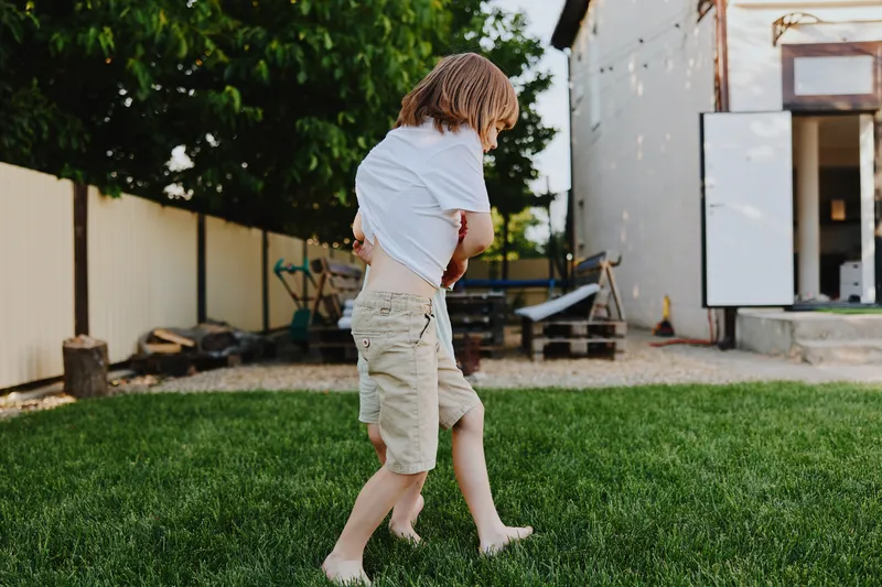 Joyful boy playing in the backyard during summer, enjoying carefree moments and laughter with friends. Bright sunlight and green grass create a vibrant atmosphere.