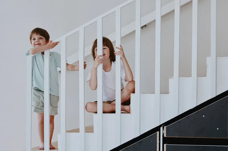 Two playful children enjoying their time on a staircase, showcasing joy and innocence, with bright colors and a minimalist background.