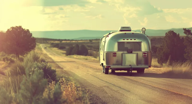 Путешествие на трейлере Airstream: закатное путешествие по проселочной дороге с заходящим вдалеке солнцем