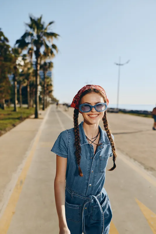 Lifestyle woman in modern boho-western denim street style wearing sunglasses and headscarf, smiling outdoors in warm natural film color light, urban summer vibe
