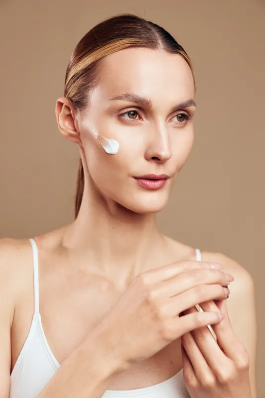 Woman applying cream on her face, closeup, skincare routine, beauty selfcare and wellness concept, moisturizer on skin, calm studio light on beige background