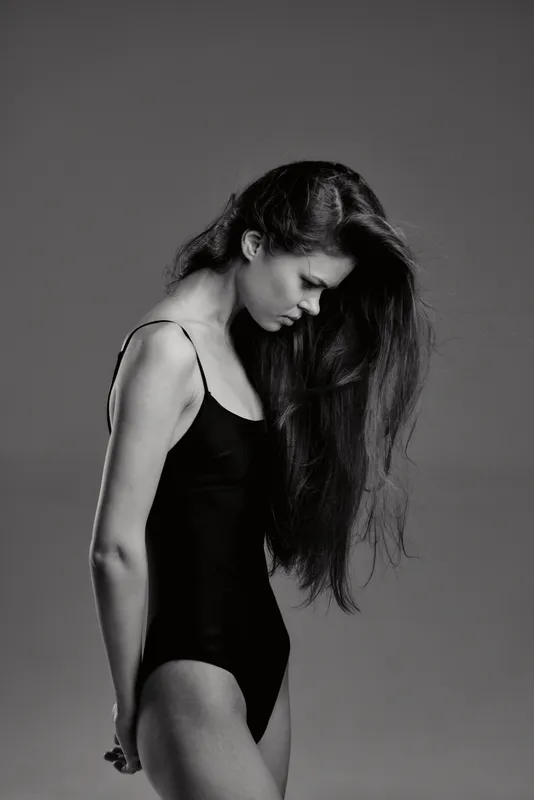 Black and white portrait of a slender woman with long hair in a swimsuit looking down thoughtfully.