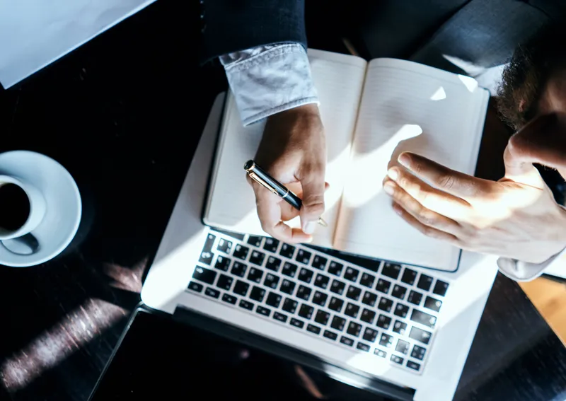 Бизнесмен сидит в кафе перед ноутбуком, документами и чашкой кофе
