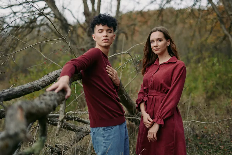 A young man and woman pose naturally in a forest clearing, conveying authenticity through genuine expressions, relaxed body language and thoughtful eye contact in a candid portrait shot.