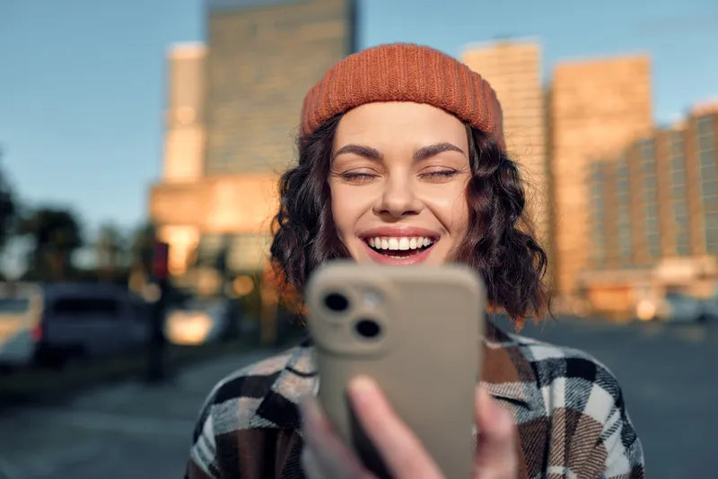 Woman smile smartphone urban beanie curlyhair golden candid young woman laughing at phone in city at golden hour glow, authenticity and mindful living vibe with emotional storytelling.
