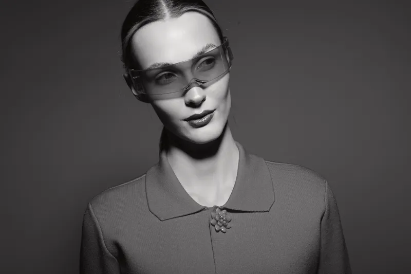Elegant white woman with fair skin wearing transparent sunglasses and a textured jacket looks aside in black and white studio portrait. Concept of fashion, style, and modern eyewear.