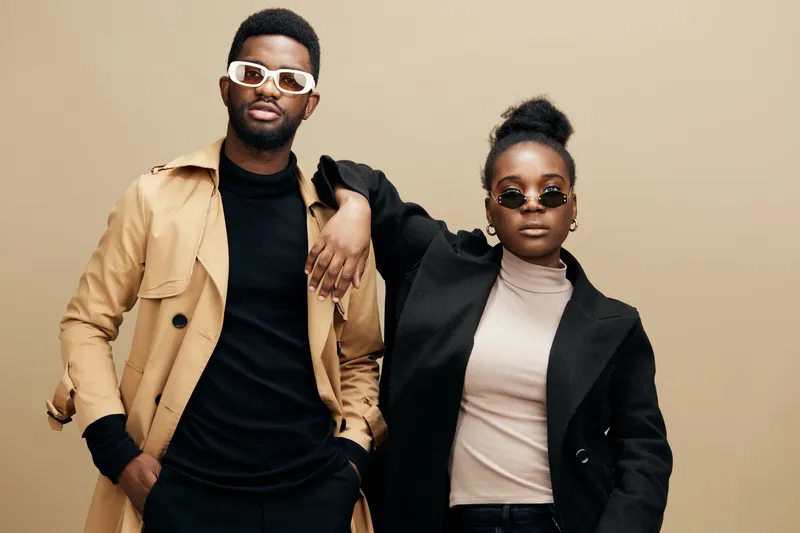 Stylish couple in neutral fashion attire posing confidently against a beige background, showcasing modern urban style and seasonal trends