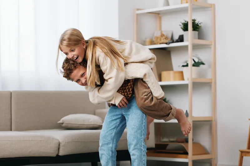 Authentic lifestyle moment at home, capturing playful affection as one person carries another in a spontaneous, joyful gesture that conveys warmth, comfort, and genuine connection.