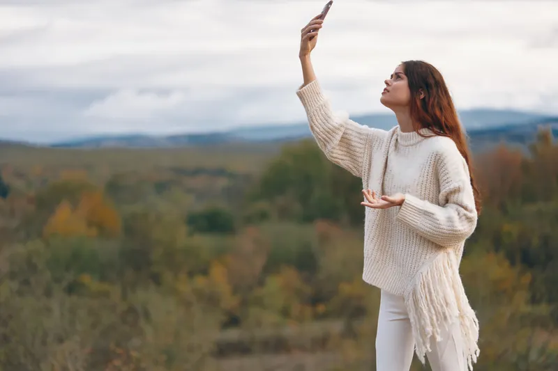 Женщина в горах: улыбающаяся любительница приключений в походе, делающая селфи на мобильный телефон на фоне прекрасного природного пейзажа
