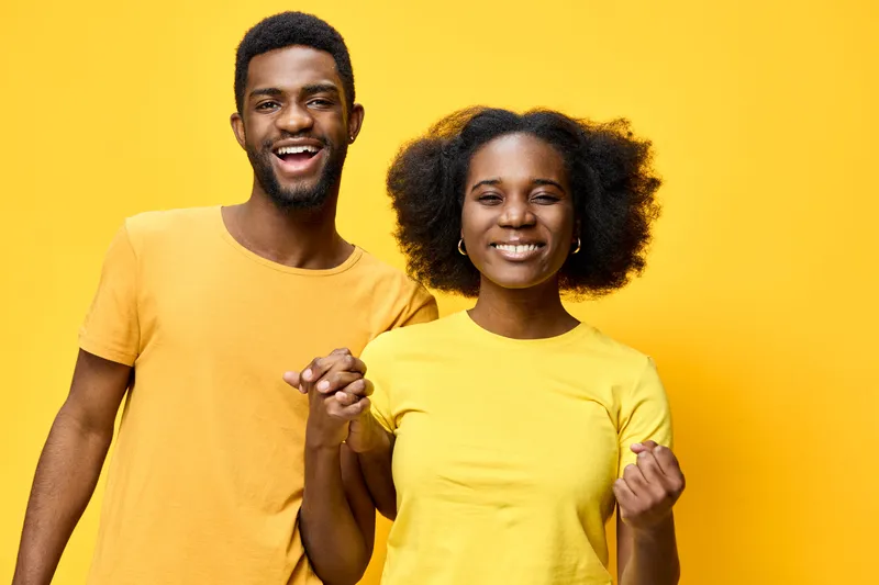 Happy African American couple wearing yellow shirts, expressing joy and positivity against a bright yellow background, perfect for lifestyle and relationship themes