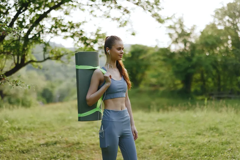 Fit young woman with a yoga mat in athletic wear enjoying nature in a green park, expressing tranquility and health focused lifestyle
