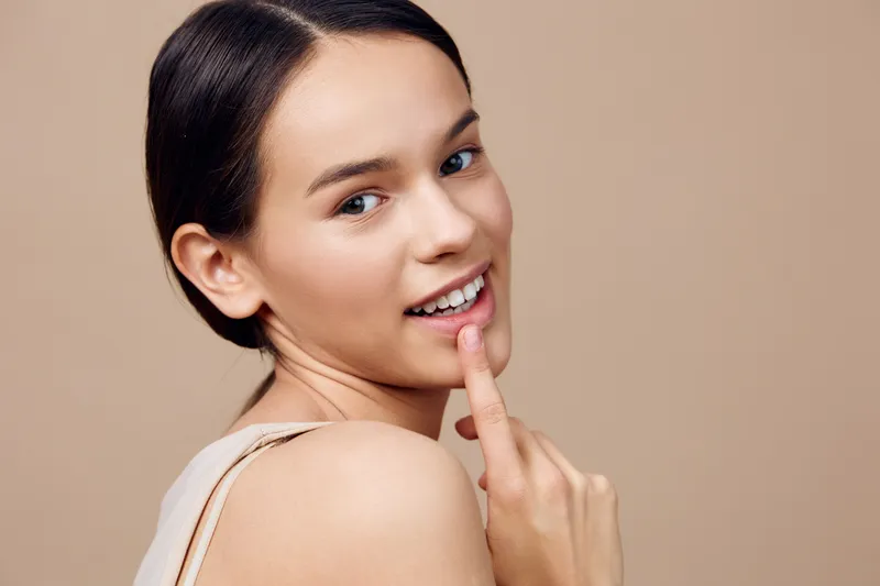 Young woman with a warm smile on a neutral background, showcasing natural beauty and confidence, ideal for wellness and beauty concepts