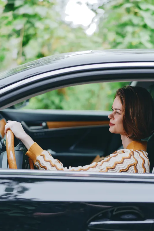 A woman drives a sleek car, hands on the wheel, focused on the road inside a modern vehicle.