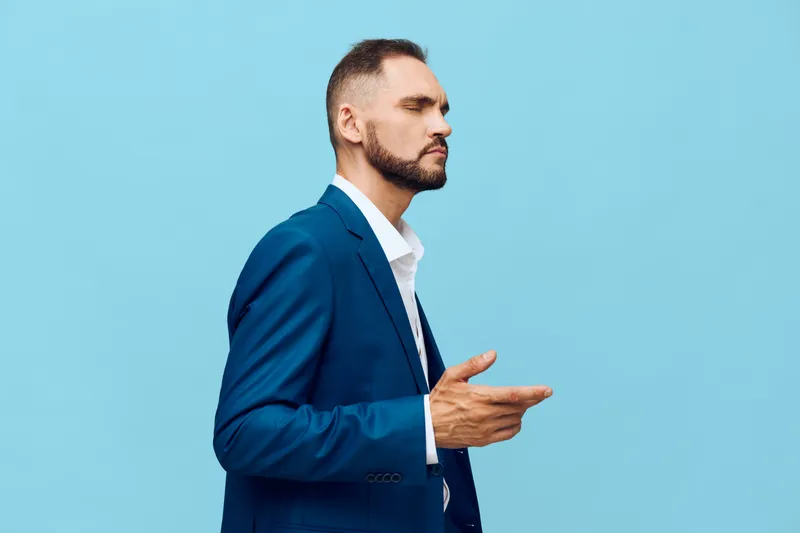 A professional man in a blue suit stands in profile against a solid blue backdrop, projecting confidence and focus as he gestures thoughtfully.