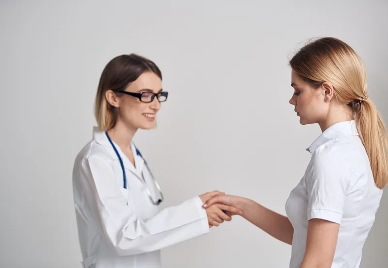 Профессиональная женщина-врач и пациент пожимают друг другу руки на светлом фоне