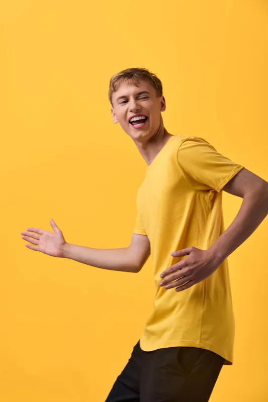 Joyful young man in a bright yellow shirt dances against a vivid yellow backdrop, conveying energy, movement, and a cheerful mood suitable for lifestyle, entertainment and dynamic advertising scenes