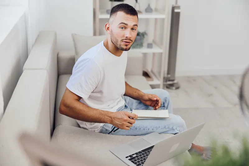 Focused man working on a laptop at home, showcasing a modern lifestyle, creativity, and productivity in a cozy environment.