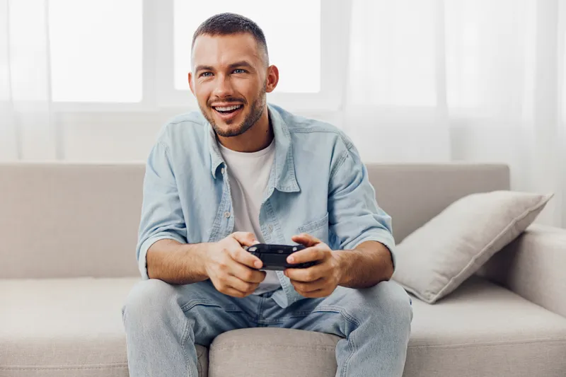Enjoyable moment with a smiling man playing video games, showcasing a cozy indoor setting filled with joy and relaxation.