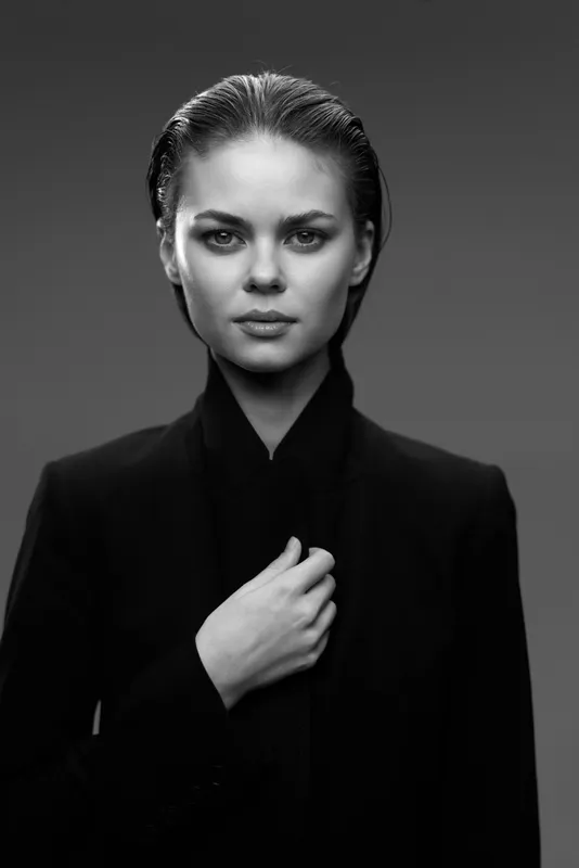 Black and white portrait of serious woman in dark clothing with confident expression and hand near collar