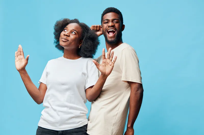 Joyful young African American couple celebrating together in a vibrant blue background, expressing fun and happiness with stylish casual outfits