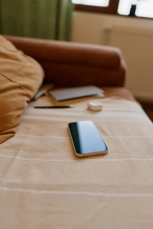 Woman relaxing at home, lying on a bed with a smartphone nearby, casual cozy vibe, soft natural light, neat living space, everyday lifestyle moment indoors.