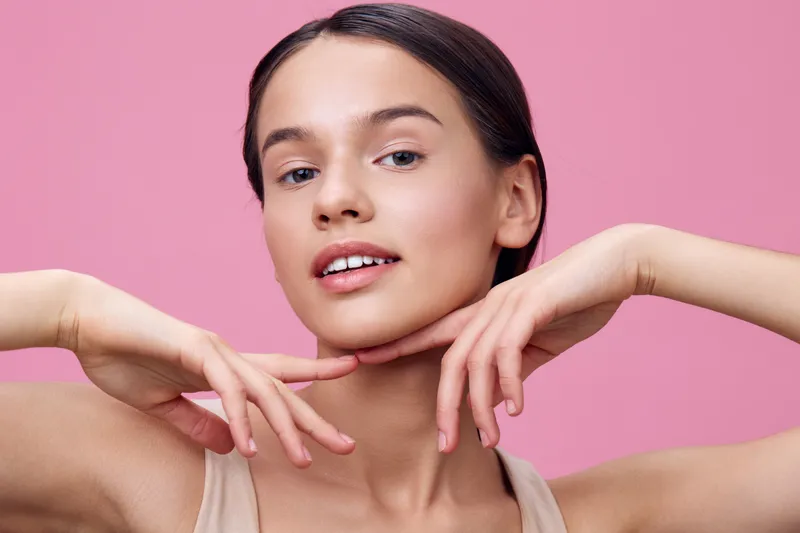 Young woman with natural makeup posing against a pink background, showcasing beauty and confidence, perfect for health and wellness concepts