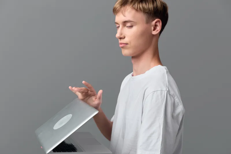 Young man with a laptop in hand, showcasing modern tech use and casual workspace vibe, focused expression, clean gray backdrop, everyday computing and remote work scenario
