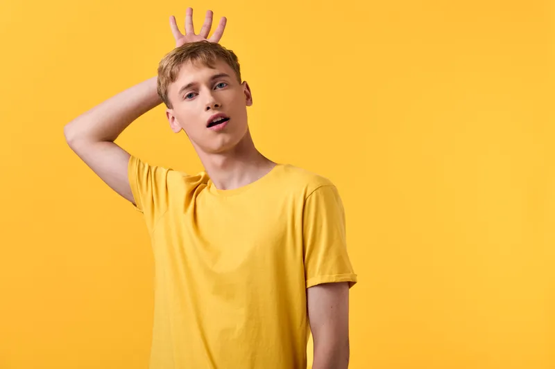 Male in yellow shirt makes bunny ears gesture in a bright studio, playful expression and dynamic pose, capturing a fun lifestyle moment with bold color and energetic vibe