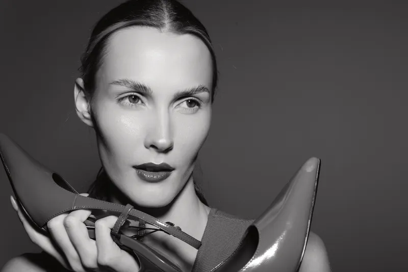 Closeup of a young white woman holding high heel shoe near face with soft studio lighting on dark background.
