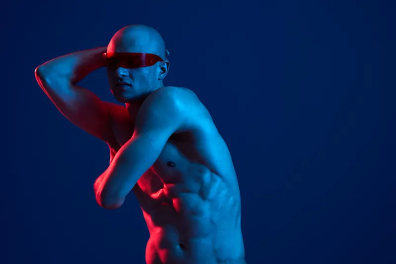 A striking image of a man posing creatively, featuring bold lighting and a futuristic aesthetic that captures his toned physique and unique style in blue and red hues.