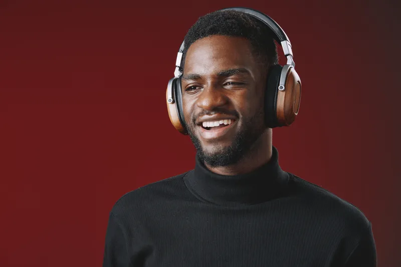 Smiling young black man in headphones against a red background, showcasing joy and connection through music, ideal for lifestyle and technology concepts