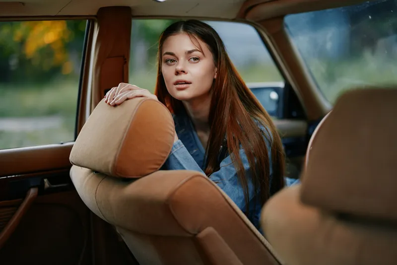 Young woman with long hair in a cozy car interior, wearing a denim jacket, looking thoughtfully out of the window, capturing a serene and contemplative moment.