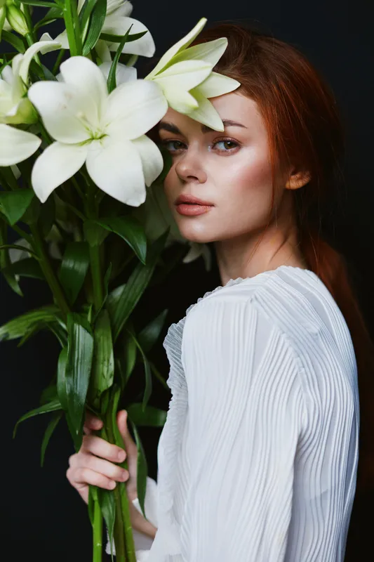 Elegant portrait of a female model holding white lilies a serene expression against a dark background, showcasing beauty and grace in a minimalistic style