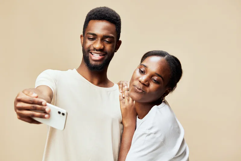 Happy couple taking a selfie together, smiling warmly against a light beige background, sharing a joyful moment and creating lasting memories