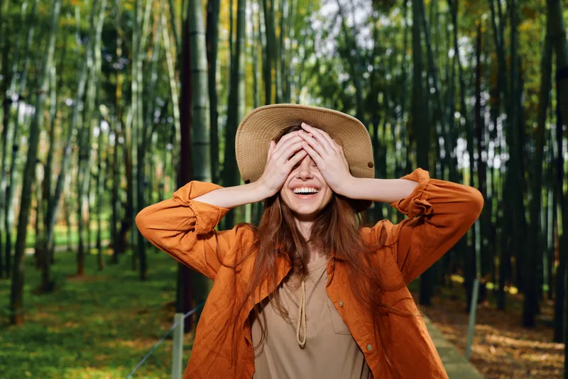 Woman smile hat bamboo nature outdoors happiness portrait, candid image of a young traveler covering her eyes with a straw hat in a green bamboo forest enjoying sunlight and autumn style